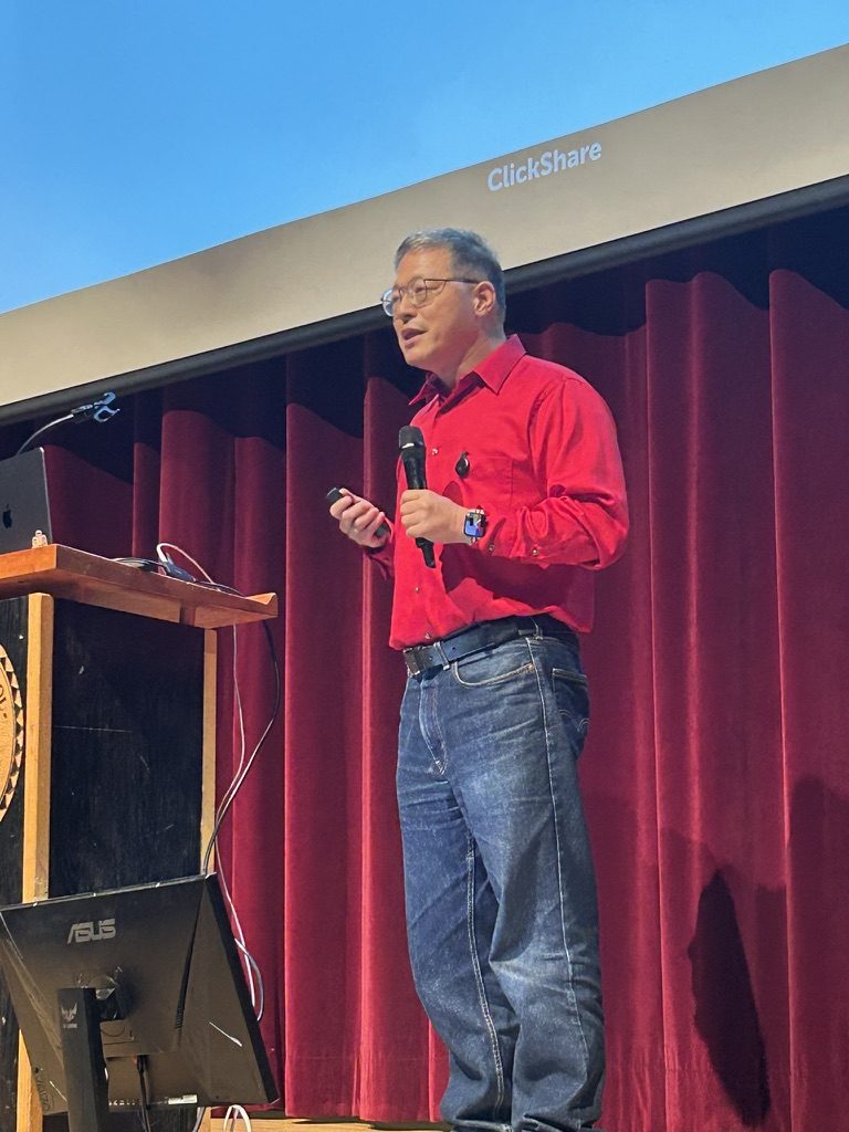 Douglas Kiang speaking on stage, holding a microphone